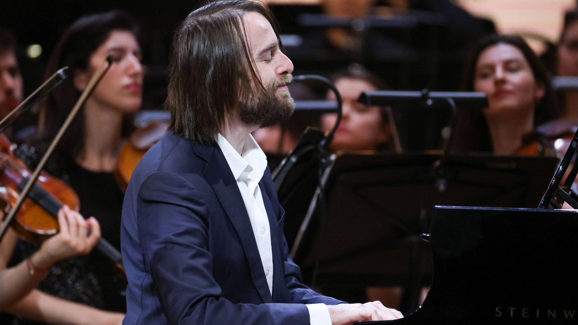 Der Pianist trägt lange Haare und Bart. Er spielt auf einem Steinway Flügel, im Hintergrund sind weitere Musiker zu sehen.