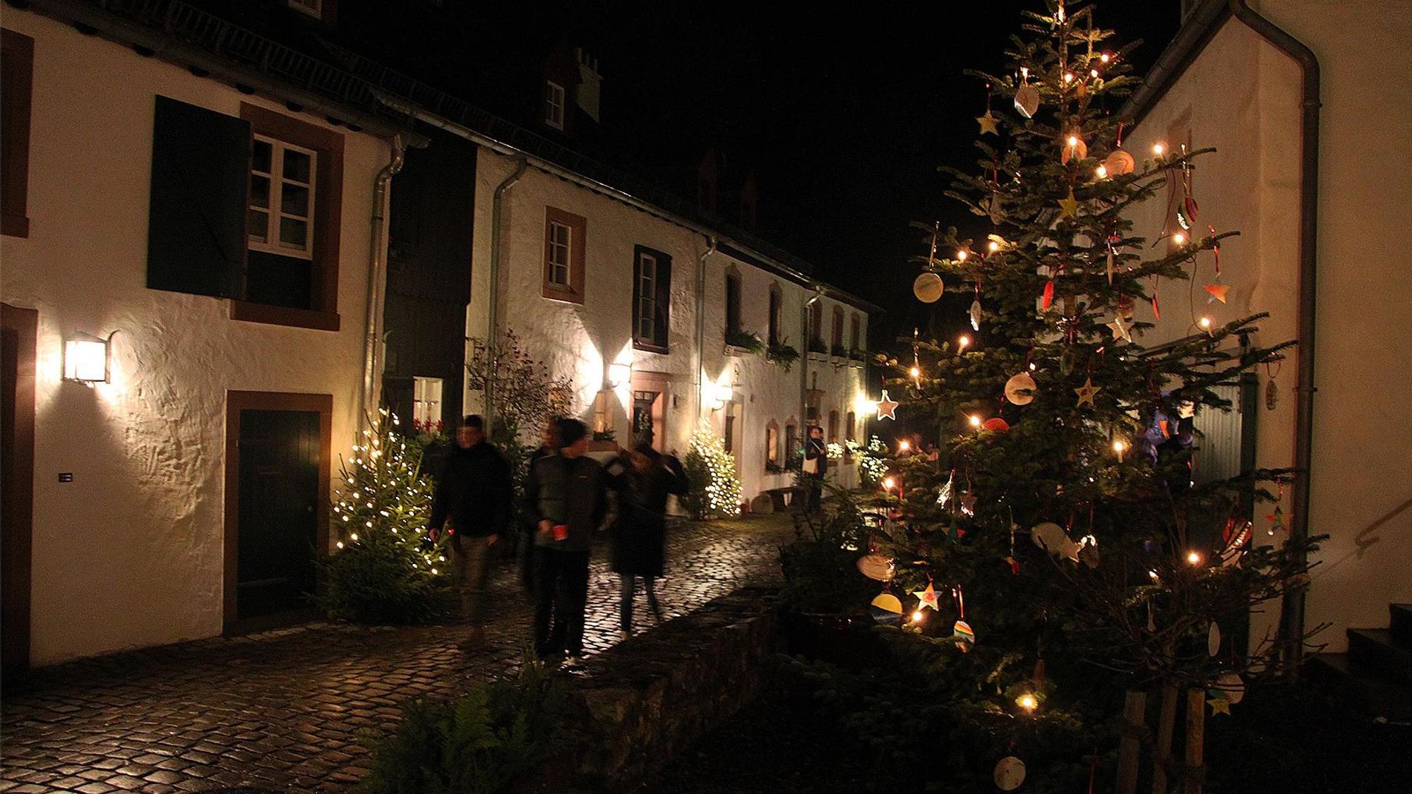 Besucher schlendern an stimmungsvoll geschmückten Weihnachtsbäumen durch die historischen Gassen von Kronenburg.