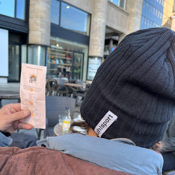 Mariam, der in einer Kölner Notunterkunft lebt, zeigt eine Zahlungsaufforderung der KVB wegen Schwarzfahrens. Man sieht nur Schultern und Hinterkopf des Mannes, der unerkannt bleiben möchte, und den Zettel mit der Zahlungsaufforderung.