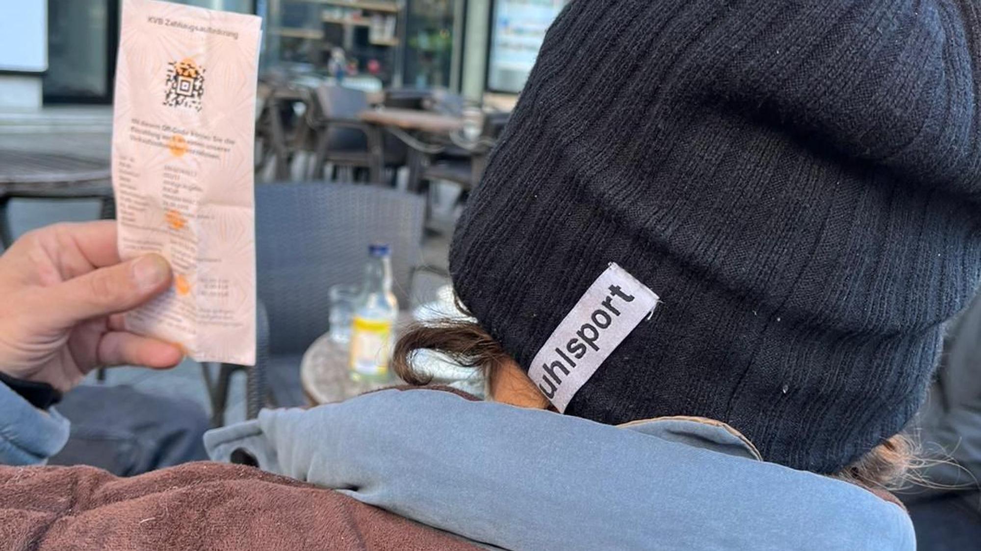 Mariam, der in einer Kölner Notunterkunft lebt, zeigt eine Zahlungsaufforderung der KVB wegen Schwarzfahrens. Man sieht nur Schultern und Hinterkopf des Mannes, der unerkannt bleiben möchte, und den Zettel mit der Zahlungsaufforderung.