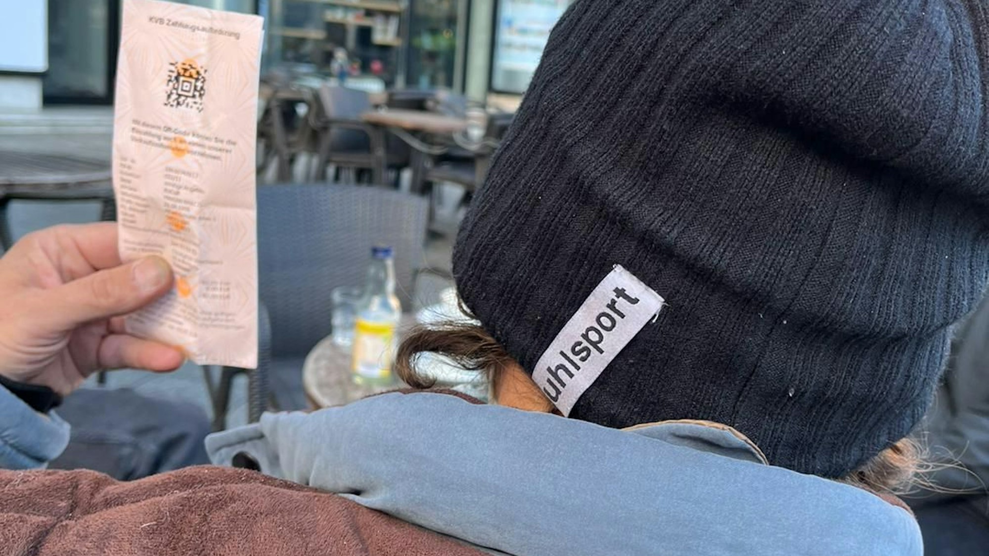 Mariam, der in einer Kölner Notunterkunft lebt, zeigt eine Zahlungsaufforderung der KVB wegen Schwarzfahrens. Man sieht nur Schultern und Hinterkopf des Mannes, der unerkannt bleiben möchte, und den Zettel mit der Zahlungsaufforderung.