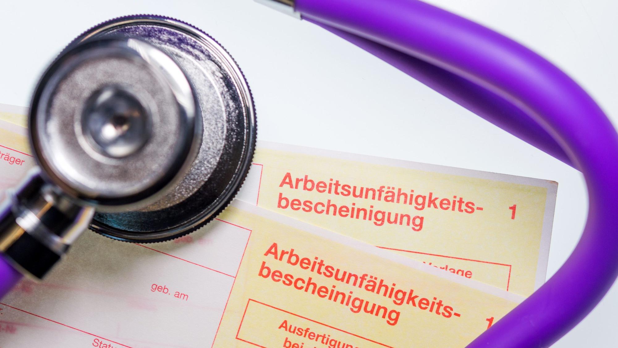 Eine Arbeitsunfähigkeitsbescheinigung und ein Stethoskop liegen auf einem Tisch.