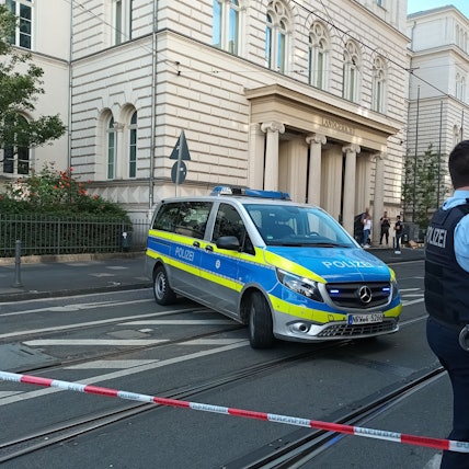 Ein Polizist und ein Streifenwagen stehen hinter einem Flatterband, mit dem der Zugang zum Landgericht Bonn abgesperrt ist.