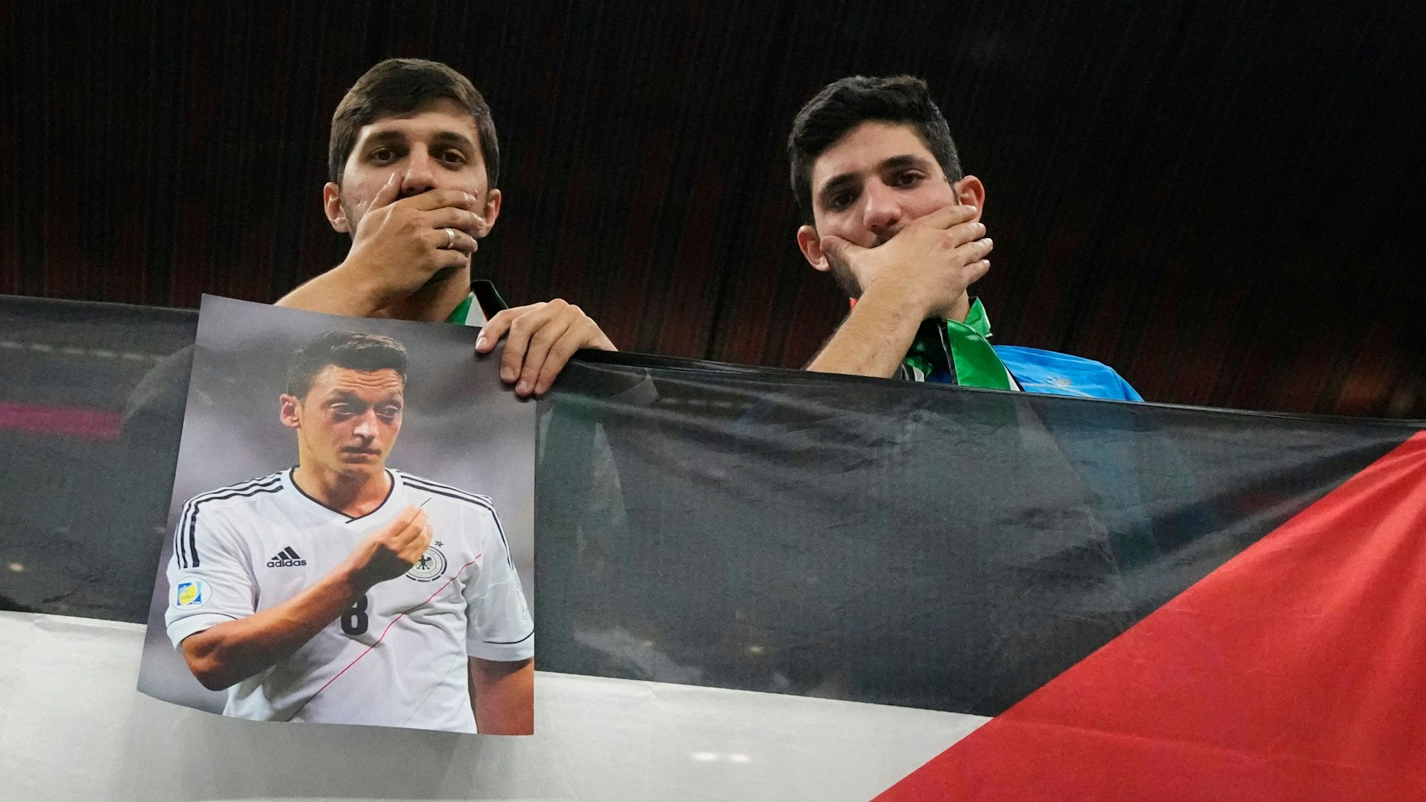 Zuschauer ahmen während der Partie gegen Spanien den deutschen Mund-zu-Protest im Stadion nach und zeigen ein Bild von Mesut Özil.