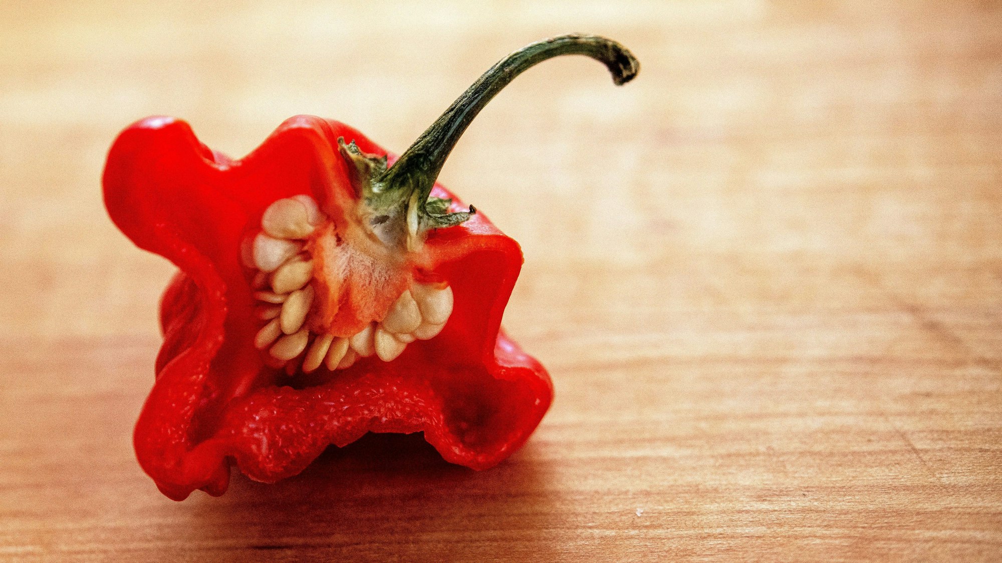 Eine aufgeschnittene Chilischote mit dem Namen „Carolina Reaper liegt auf Holz.