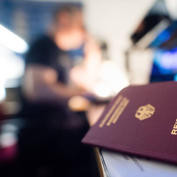 Ein deutscher Reisepass liegt in einem Labor der Kriminaltechnik der Bundespolizei am Flughafen, während im Hintergrund ein Urkundenprüfer der Bundespolizei an einem Mikroskop arbeitet.