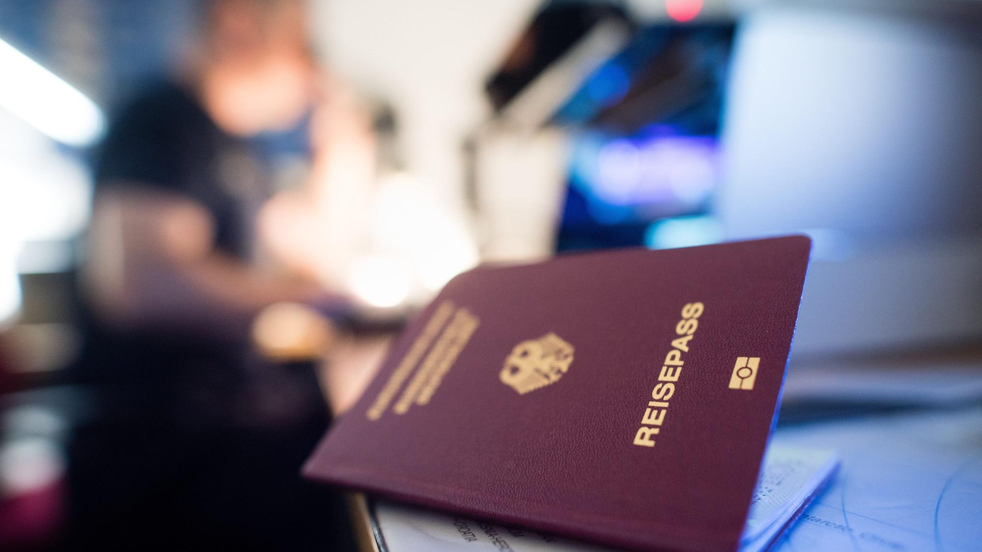 Ein deutscher Reisepass liegt in einem Labor der Kriminaltechnik der Bundespolizei am Flughafen, während im Hintergrund ein Urkundenprüfer der Bundespolizei an einem Mikroskop arbeitet.