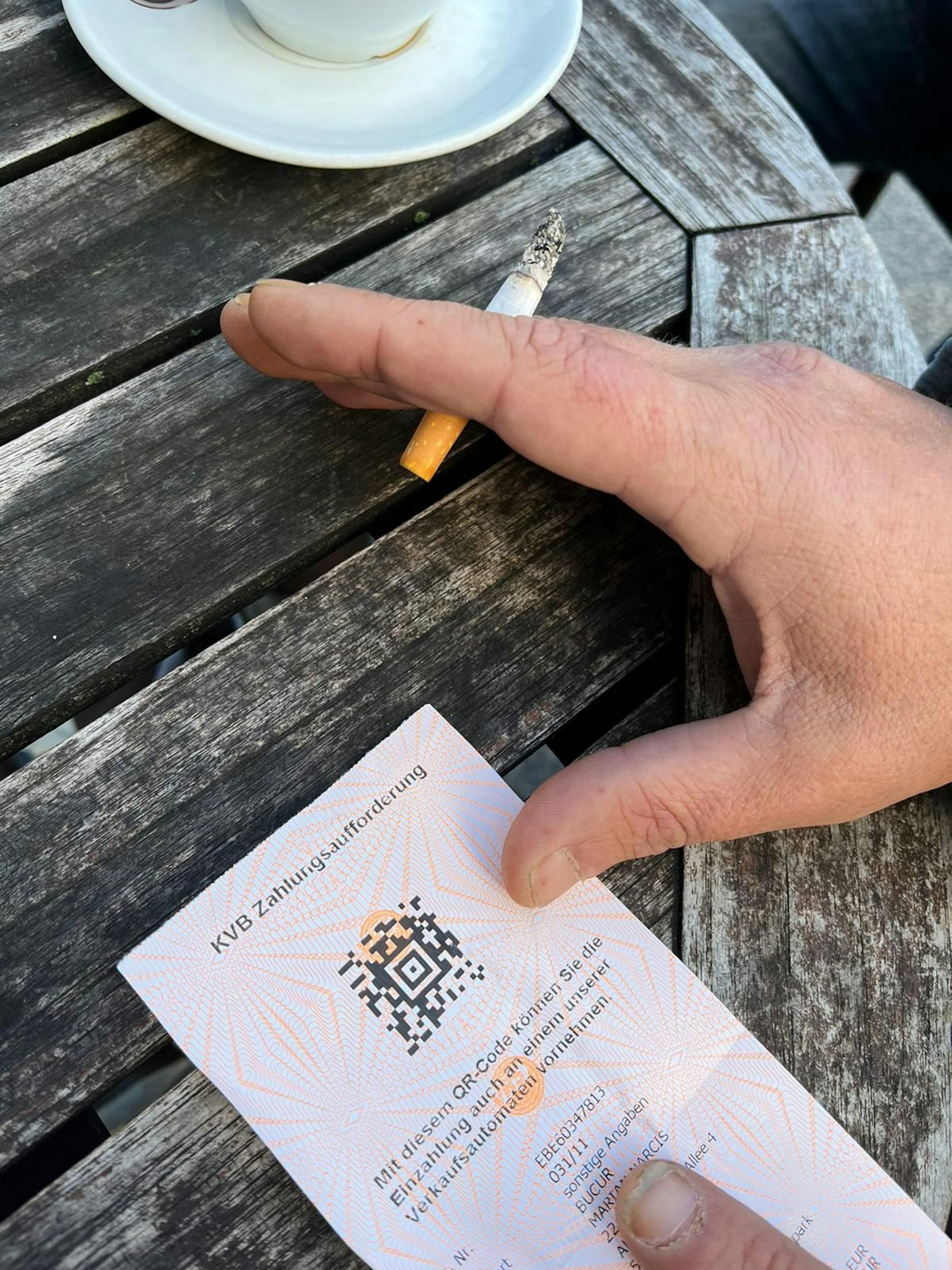 Auf dem Bild ist eine Hand von Mariam zu sehen, einem 46-Jährigen Kölner, der viermal wegen Schwarzfahrens im Gefängnis saß. Dazu ein Zettel mit einer Zahlungsaufforderung der Köner Verkehrsbetriebe.