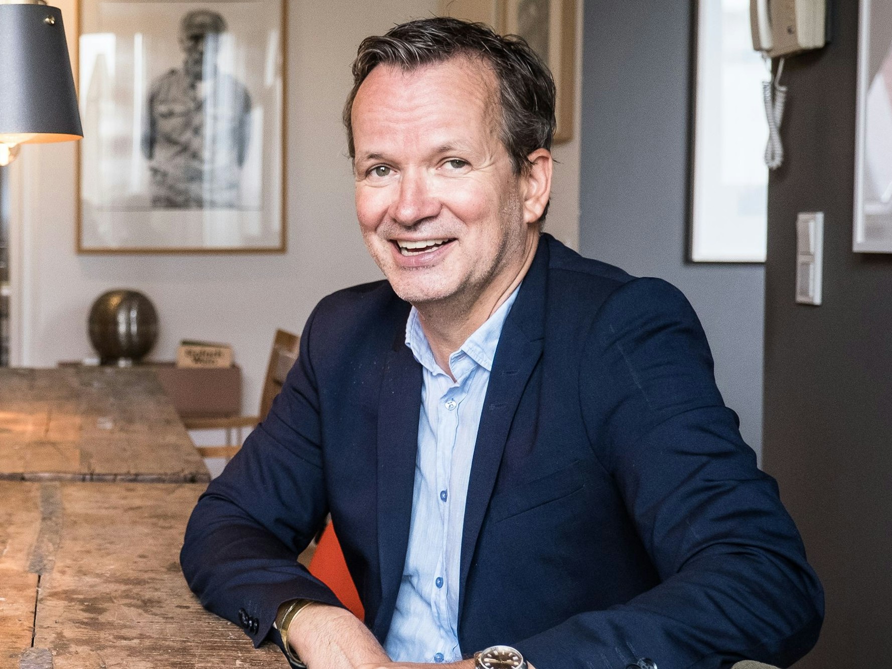 Matthias Rincón sitzt an einem Holztisch und lacht in die Kamera.