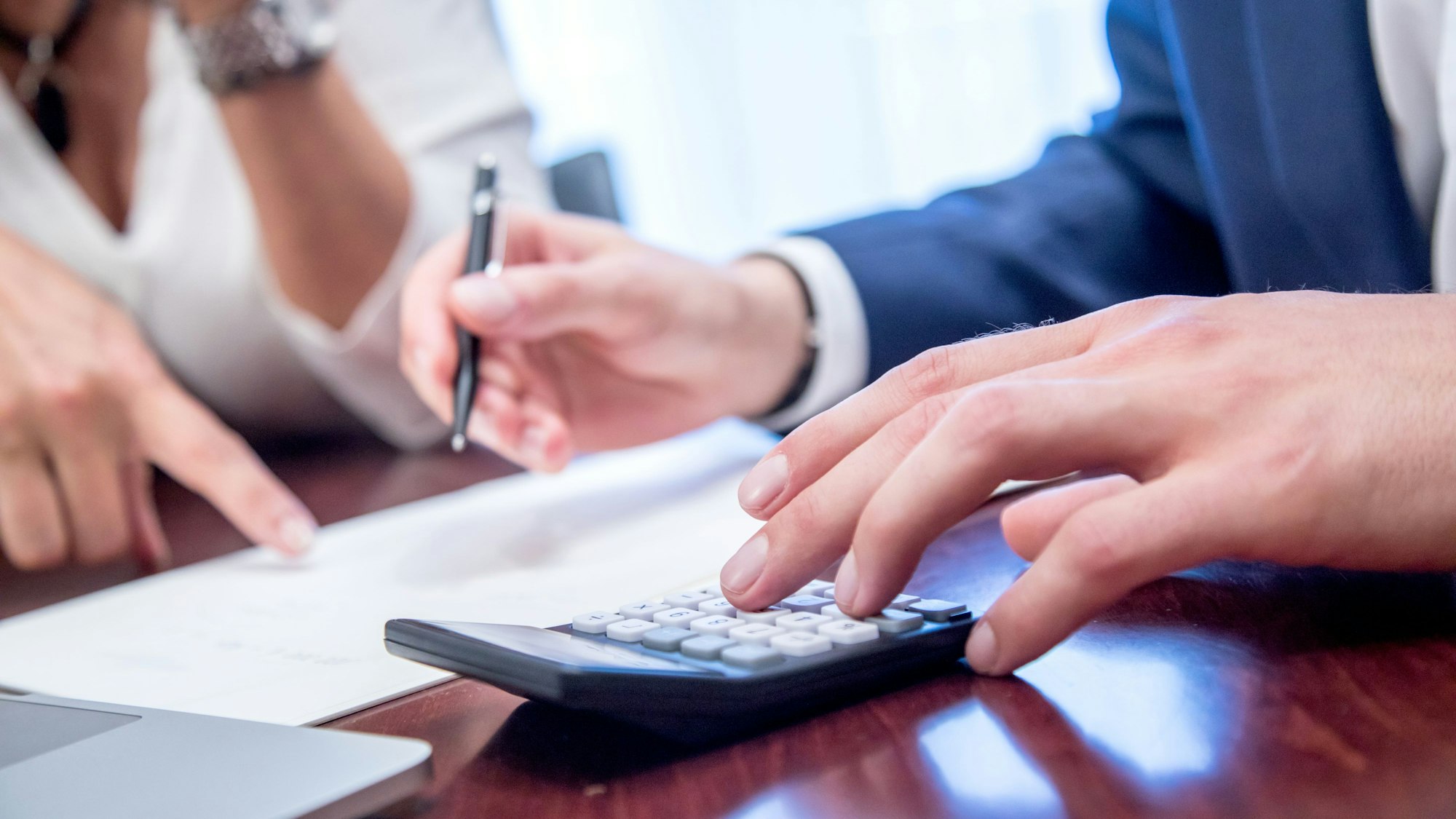 Zwei Personen sitzen mit Taschenrechner vor Papieren und schreiben.