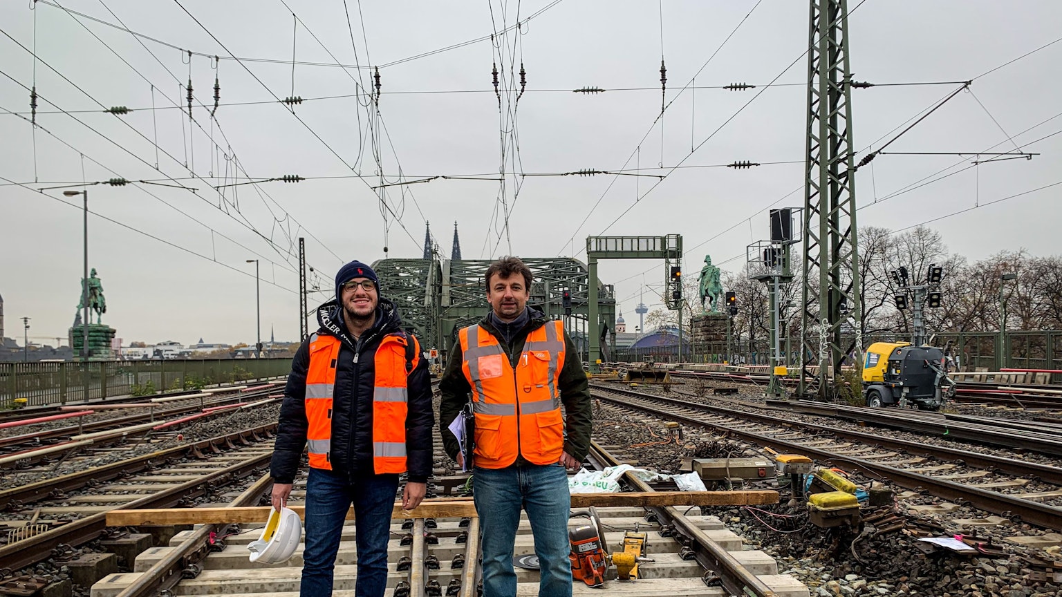 Zwei Männer stehen im Gleisbett auf der Hohenzollernbrücke: Projektleiter Naim Selimovic (links) und Bauüberwacher Miroslaw Radacz. Seit einigen Tagen erneuert die Deutsche Bahn Weichen im Bahnhof Köln Messe/Deutz. Während der Arbeiten können zwei der sechs Gleise auf der Brücke nicht befahren werden.