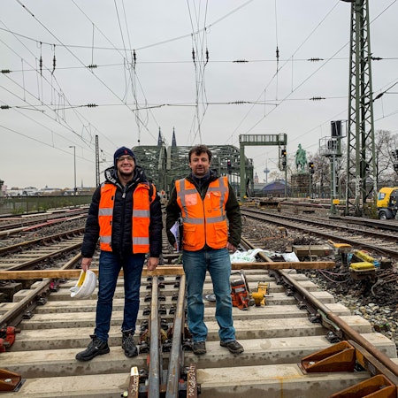 Zwei Männer stehen im Gleisbett auf der Hohenzollernbrücke: Projektleiter Naim Selimovic (links) und Bauüberwacher Miroslaw Radacz. Seit einigen Tagen erneuert die Deutsche Bahn Weichen im Bahnhof Köln Messe/Deutz. Während der Arbeiten können zwei der sechs Gleise auf der Brücke nicht befahren werden.