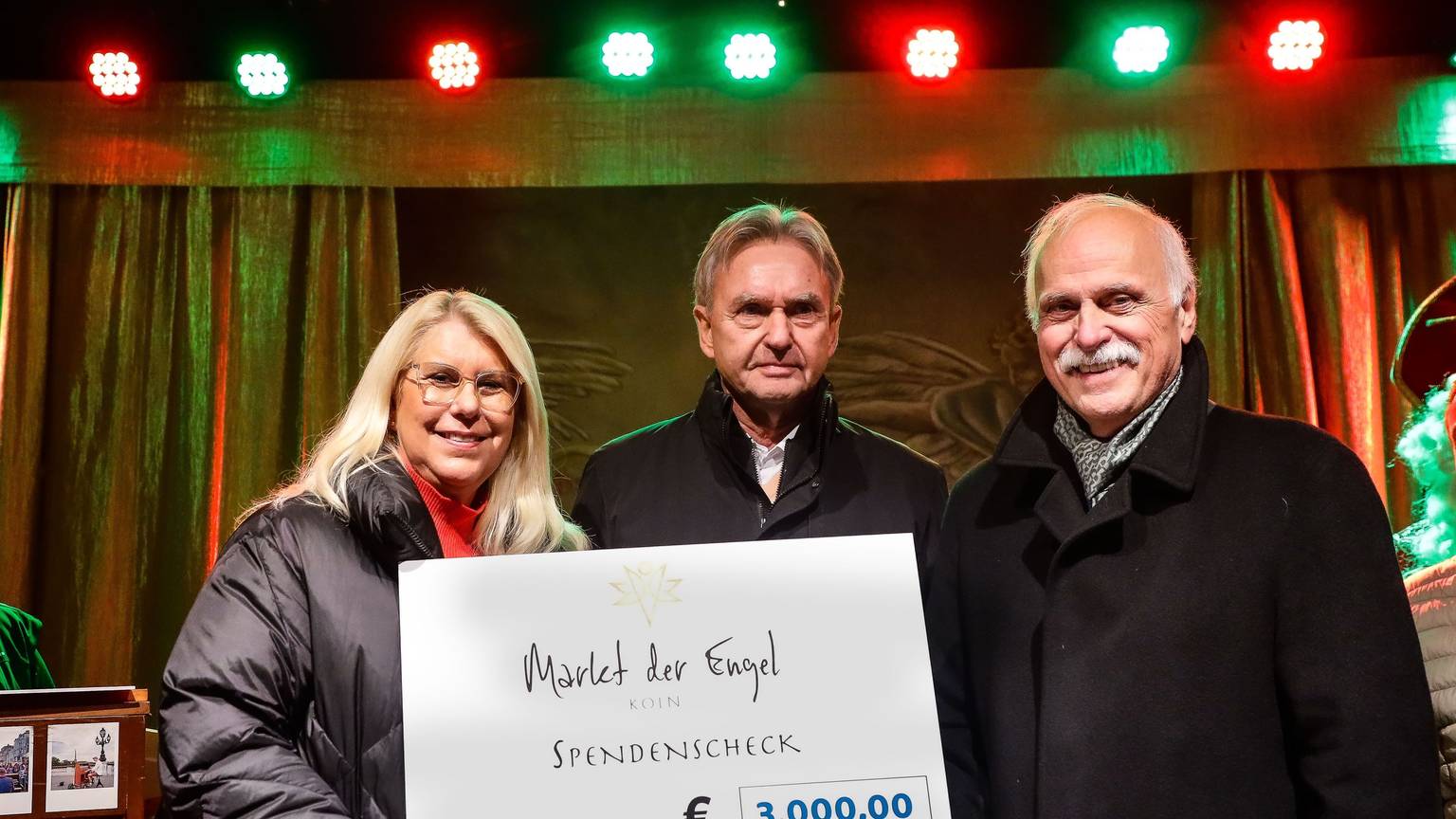 Auf der Bühne des Markts der Engel am Neumarkt überreichen die Veranstalter Herbert und Britta Putzmann dem Geschäftsführer von „wir helfen“ Karl Heinz Grossmann einen symbolischen Scheck über 3000 Euro.