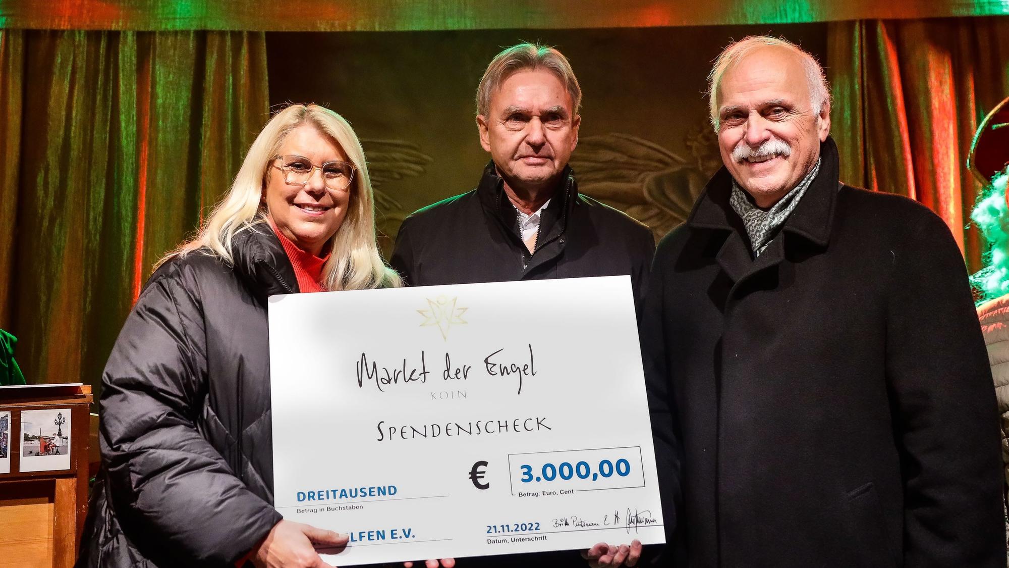 Auf der Bühne des Markts der Engel am Neumarkt überreichen die Veranstalter Herbert und Britta Putzmann dem Geschäftsführer von „wir helfen“ Karl Heinz Grossmann einen symbolischen Scheck über 3000 Euro.