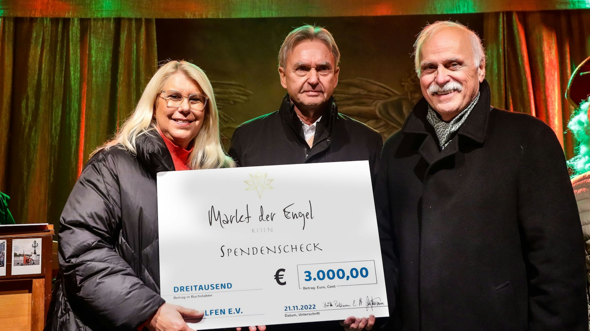 Auf der Bühne des Markts der Engel am Neumarkt überreichen die Veranstalter Herbert und Britta Putzmann dem Geschäftsführer von „wir helfen“ Karl Heinz Grossmann einen symbolischen Scheck über 3000 Euro.