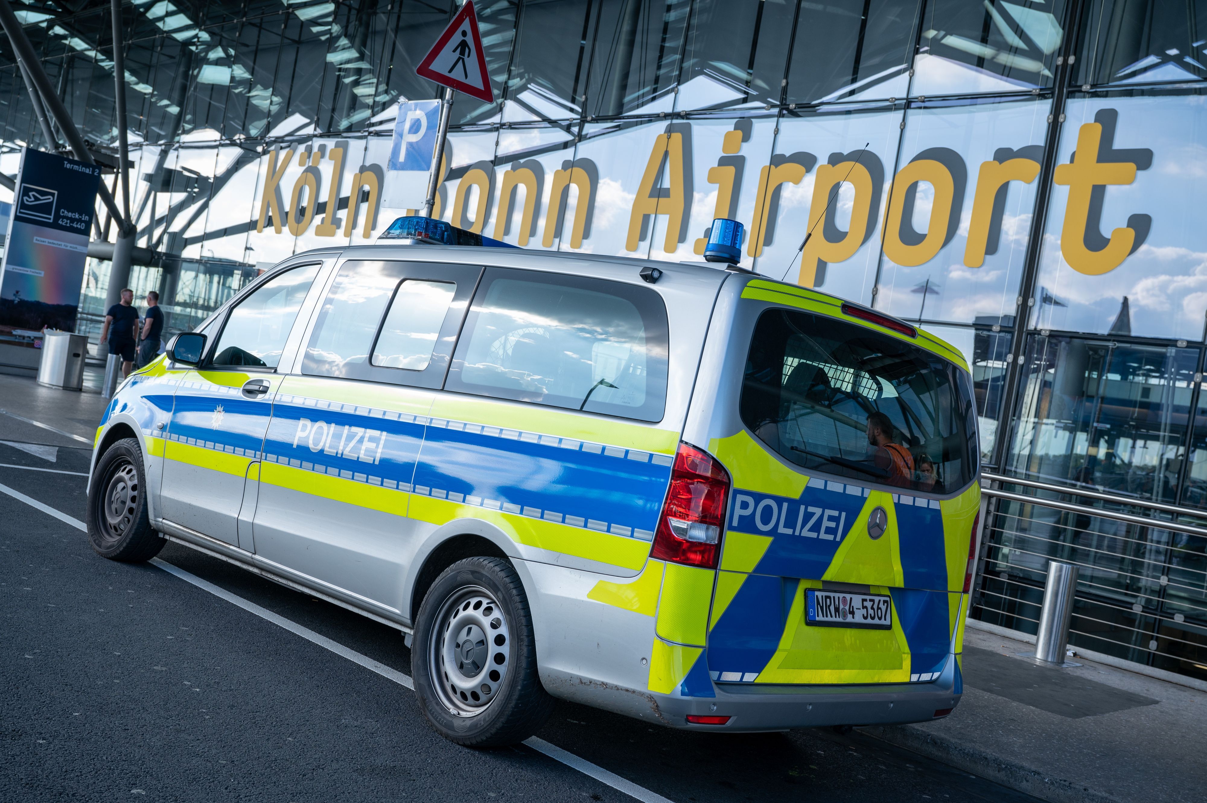 Ein Bulli der Polizei steht vor dem Flughafen Köln/Bonn. Im Hintergrund steht auf der großen Fensterfront „Köln Bonn Airport“.