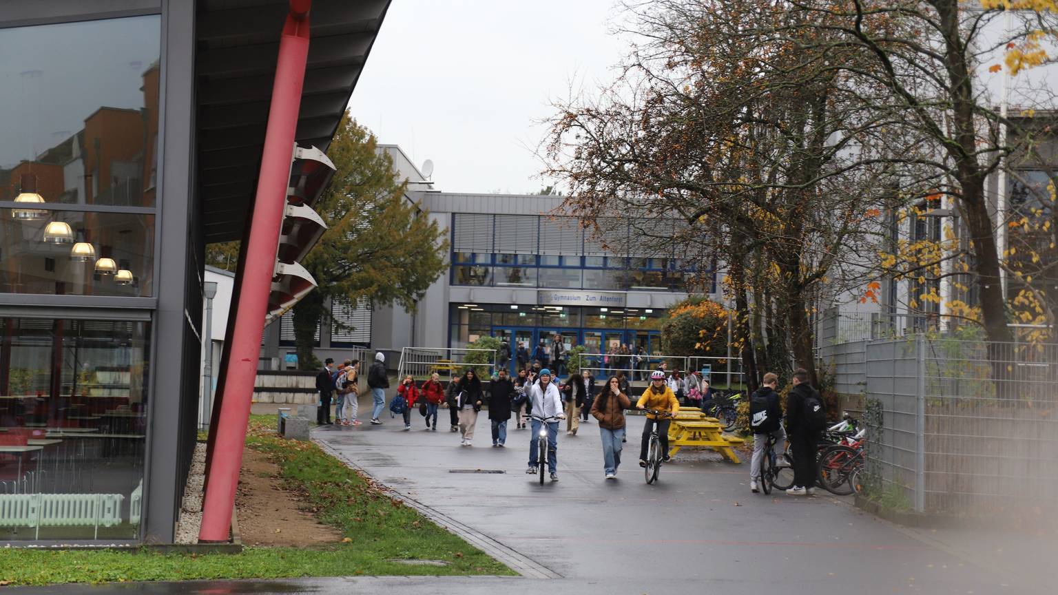 Schüler und Schülerinnen sind zu Fuß und mit dem Rad vor dem Gebäude des Gymnasiums Zum Altenforst in Troisdorf unterwegs.