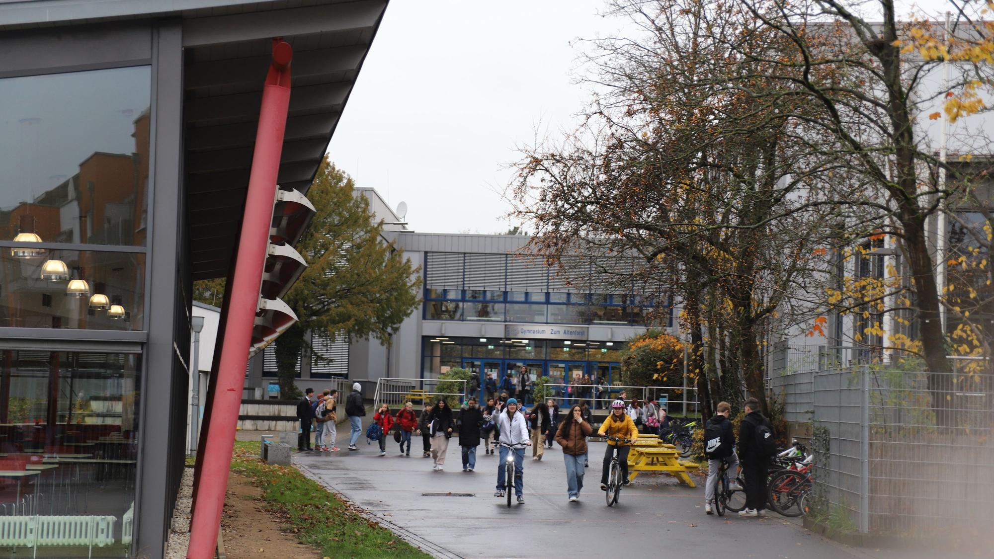 Schüler und Schülerinnen sind zu Fuß und mit dem Rad vor dem Gebäude des Gymnasiums Zum Altenforst in Troisdorf unterwegs.