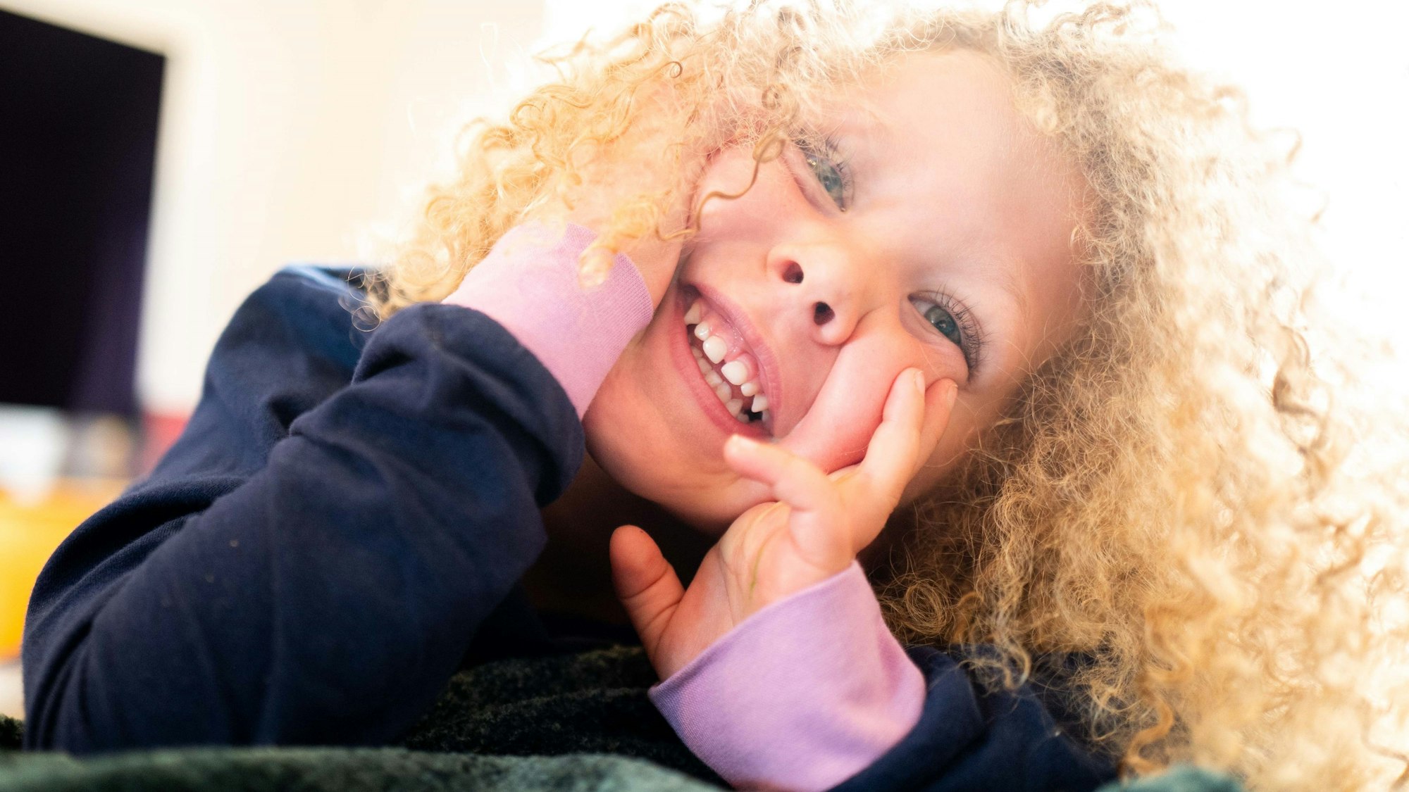 Ein Kind liegt auf einer Decke im Kindergarten und lächelt.