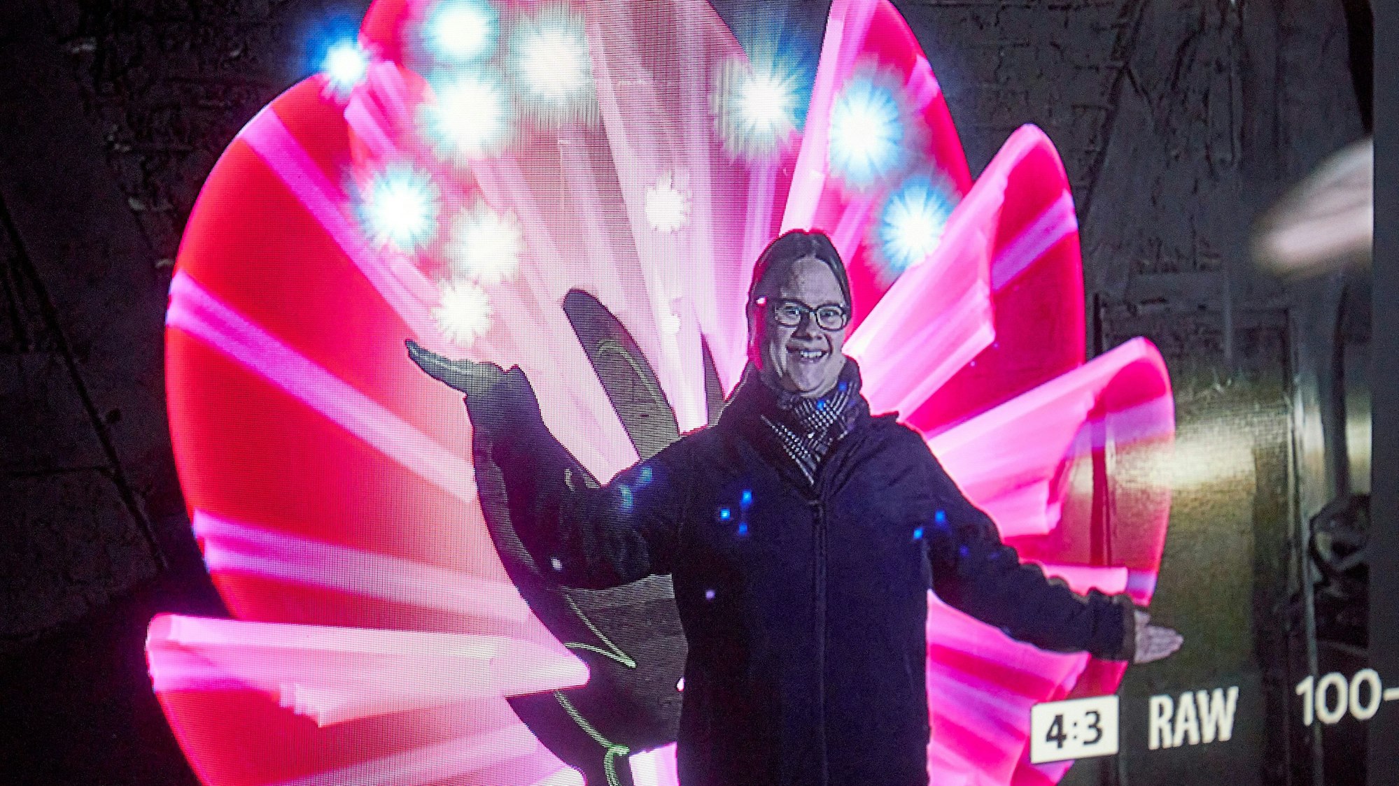 Eine Frau steht vor einer Fotowand und gestikuliert.