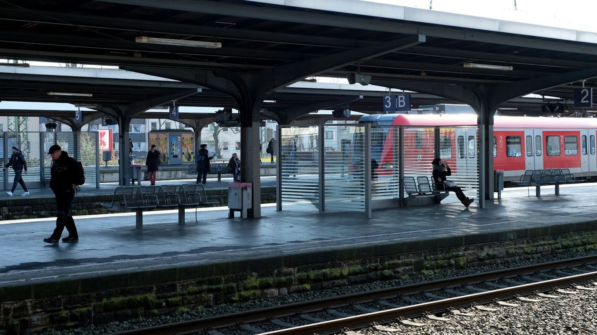 Mehrere Personen stehen und sitzen am Gleis 3 des Bahnhofs in Köln-Mülheim