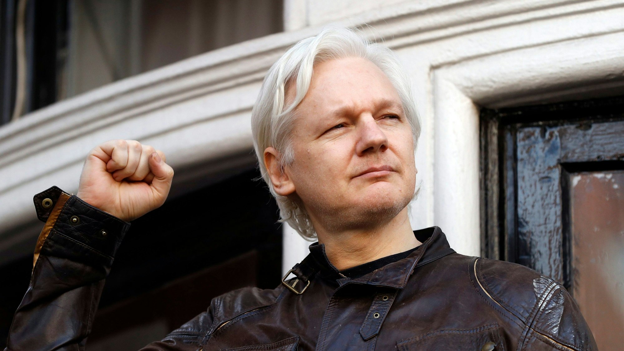 Julian Assange begrüßt 2017 Unterstützer vor der ecuadorianischen Botschaft in London. Er hebt eine Faust in die Luft.