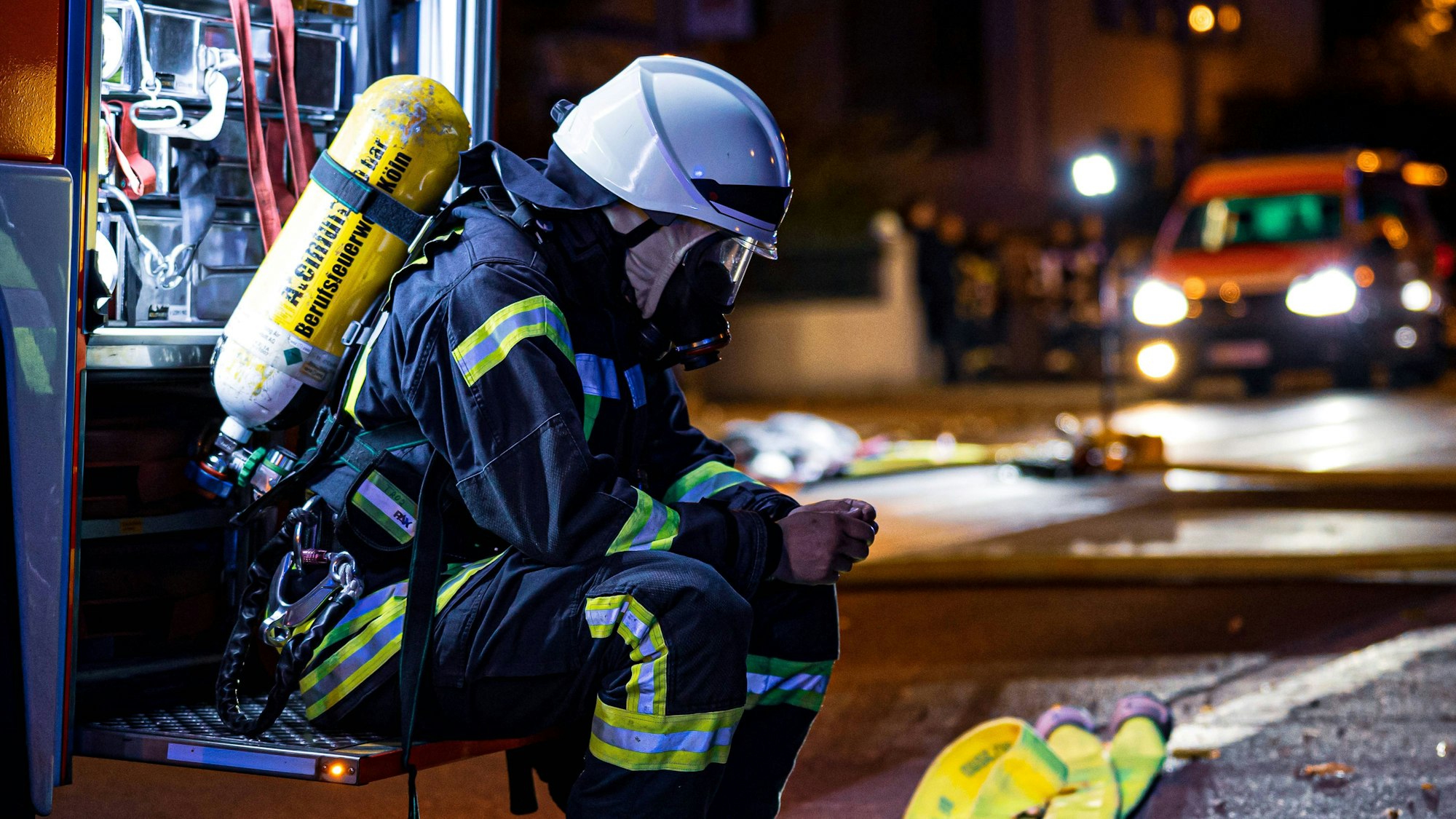 Feuerwehrmann in kompletter Ausrüstung, der vor einem Feuerwehrwagen sitzt und kurz durchatmet und innehält