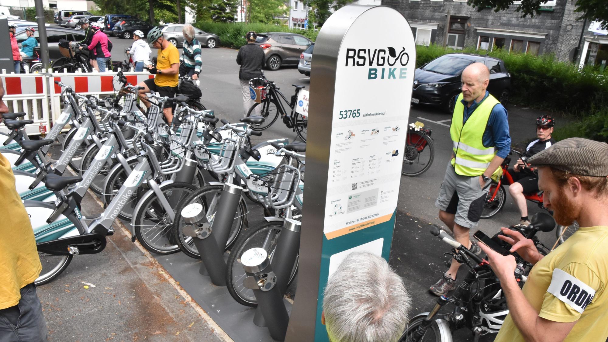 Menschen stehen um eine Stele der RSVG Bike-Vermietung herum. Dahinter sind E-Bikes aufgestellt.