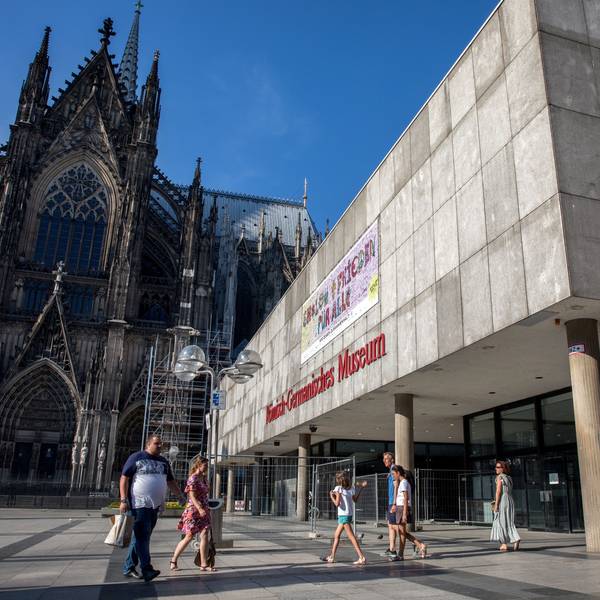 Menschen laufen über die Domplatte am Dom und dem Römisch-Germanischen Museum vorbei