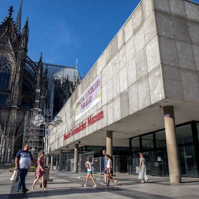 Menschen laufen über die Domplatte am Dom und dem Römisch-Germanischen Museum vorbei