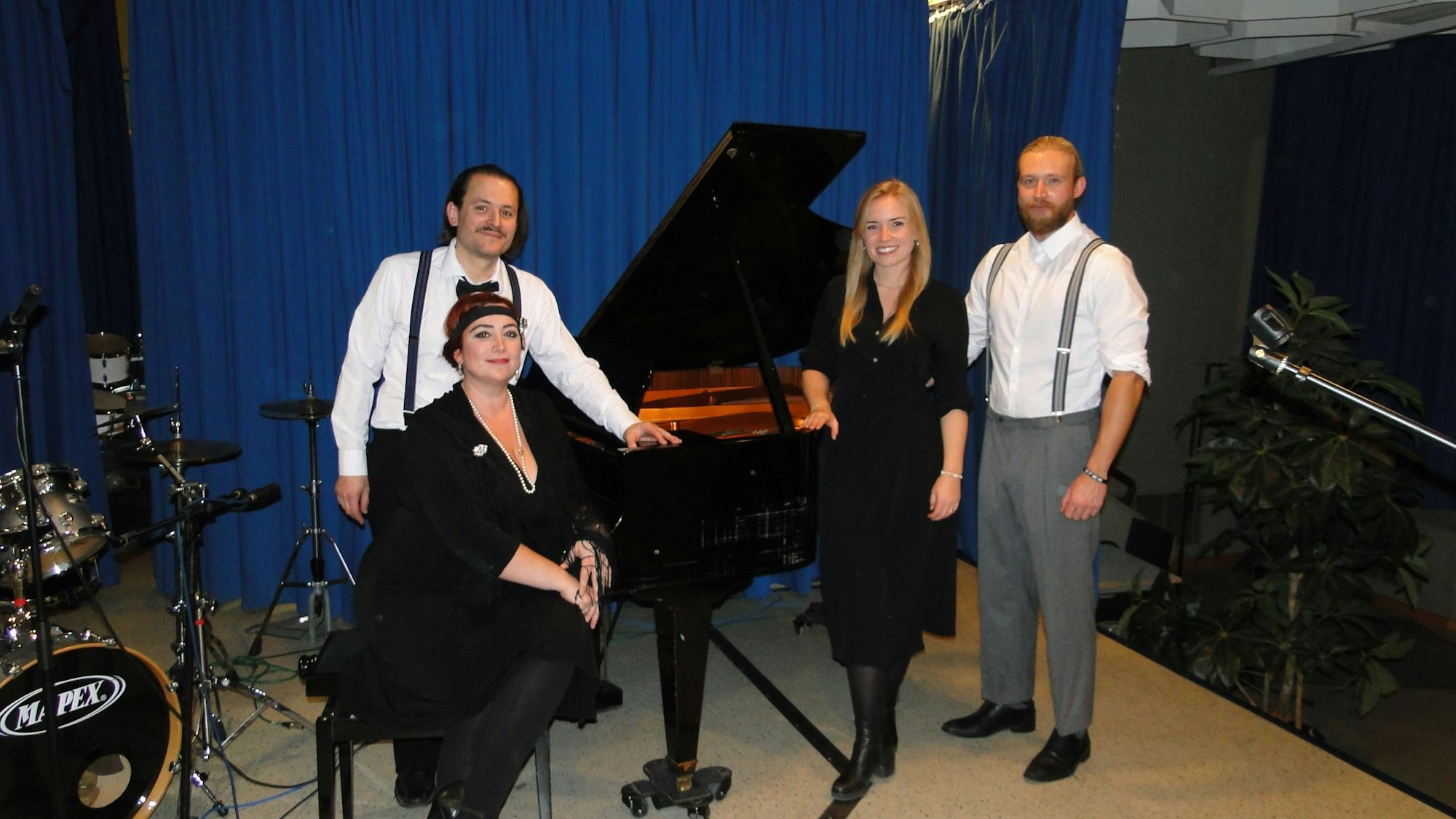 Zwei Männer und zwei Frauen im Kleidungsstil der 20er-Jahre stehen um einen Konzert-Flügel herum. Eine Dame sitzt.