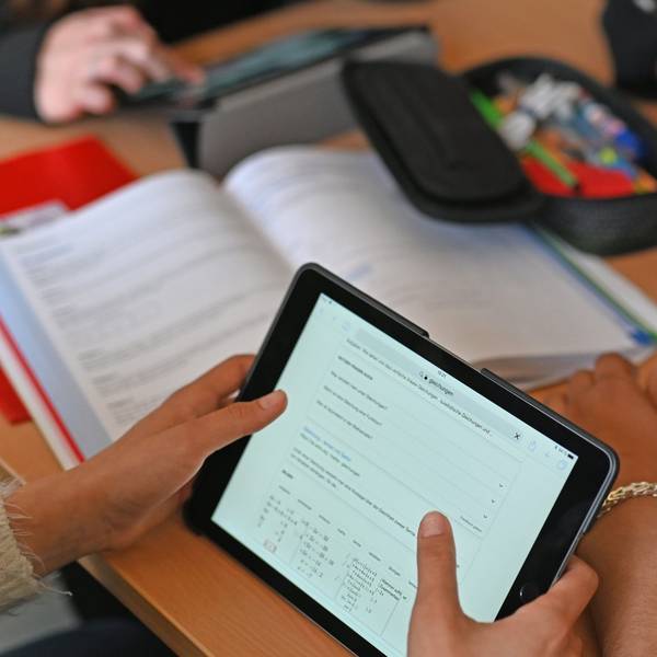 Mehrere Tablets liegen auf Schulpulten. Schüler arbeiten damit.