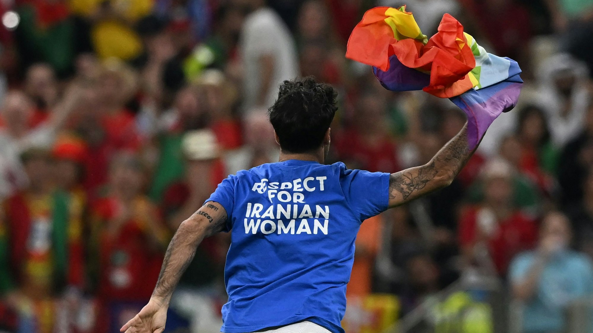 Der Italiener Marco Ferri läuft über den Rasen des Lusail-Stadions und zeigt die Regenbogenfahne. Auf der Rückseite seines T-Shirts ist zu lesen: „Respect for Iranian woman“.