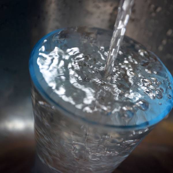 Leitungswasser fließt in ein Glas, das in einem Spülbecken steht.