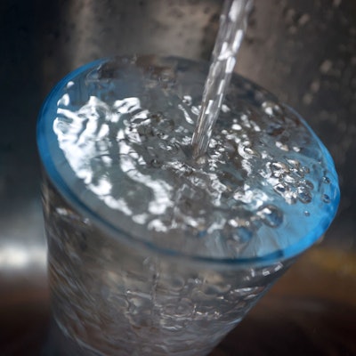 Leitungswasser fließt in ein Glas, das in einem Spülbecken steht.