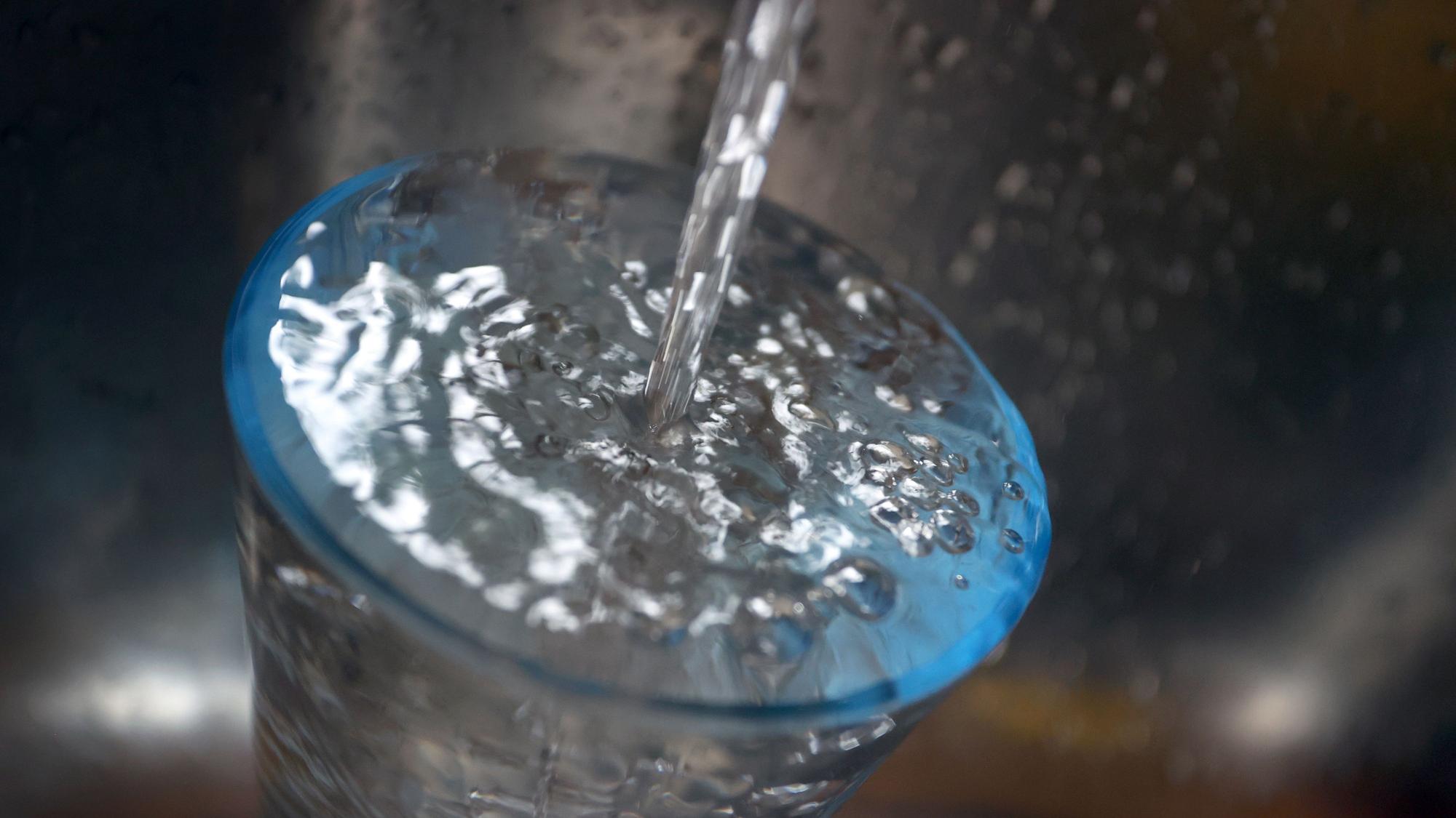 Leitungswasser fließt in ein Glas, das in einem Spülbecken steht.