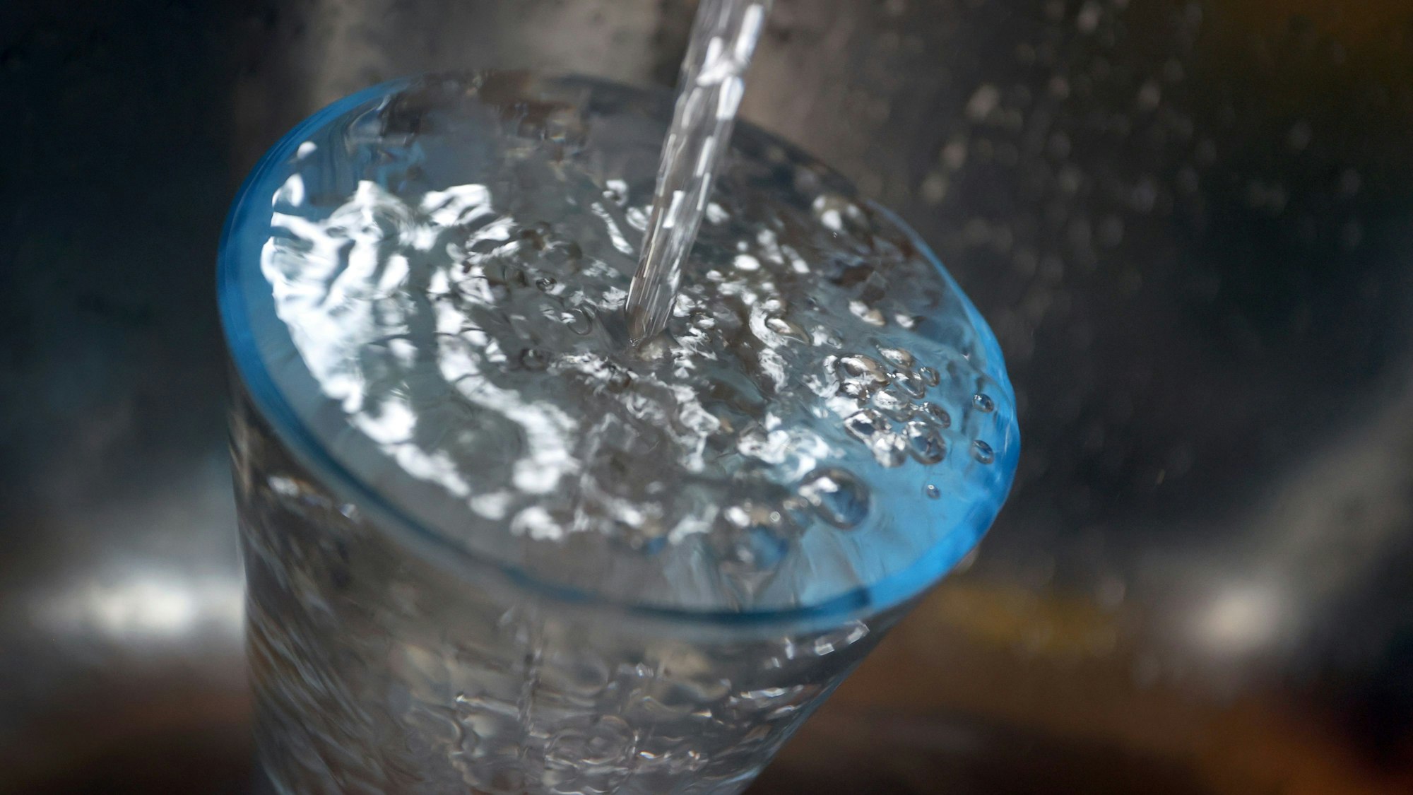 Leitungswasser fließt in ein Glas, das in einem Spülbecken steht. Der Versorger Belkaw fordert die Bürger von Bergisch Gladbach auf, sparsam mit Wasser umzugehen.