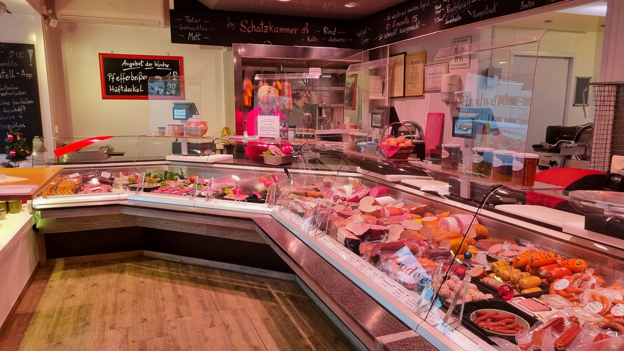 Blick in den Verkaufsraum mit bestückter Auslage in der Metzgerei von Daniel Pickartz in Leverkusen-Wiesdorf. Eine Verkäuferin steht hinter der Theke.