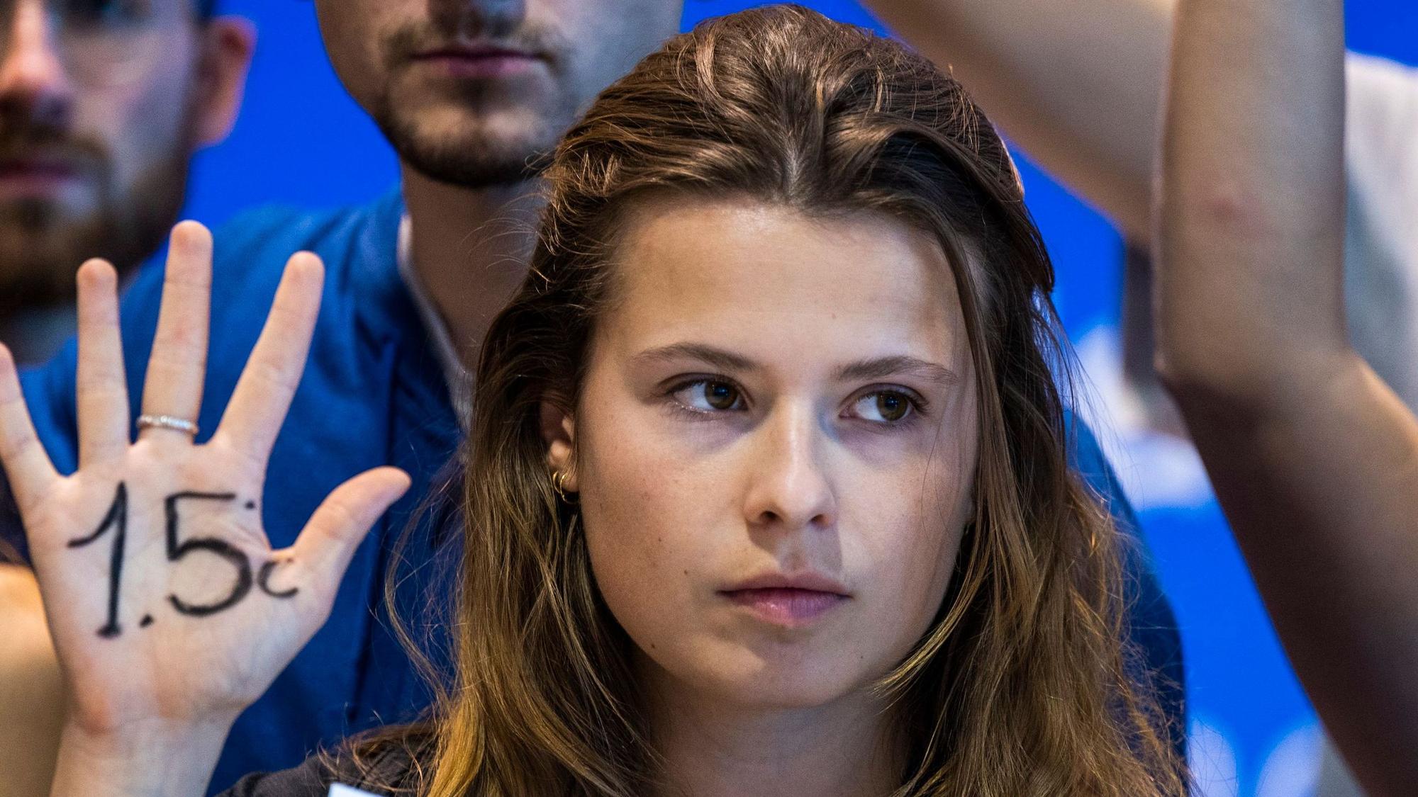 Klimaaktivistin Luisa Neubauer von „Fridays for Future“ hält eine Hand hoch, auf der „1,5 Grad“ geschrieben steht. Neubauer blickt ernst nach vorne.