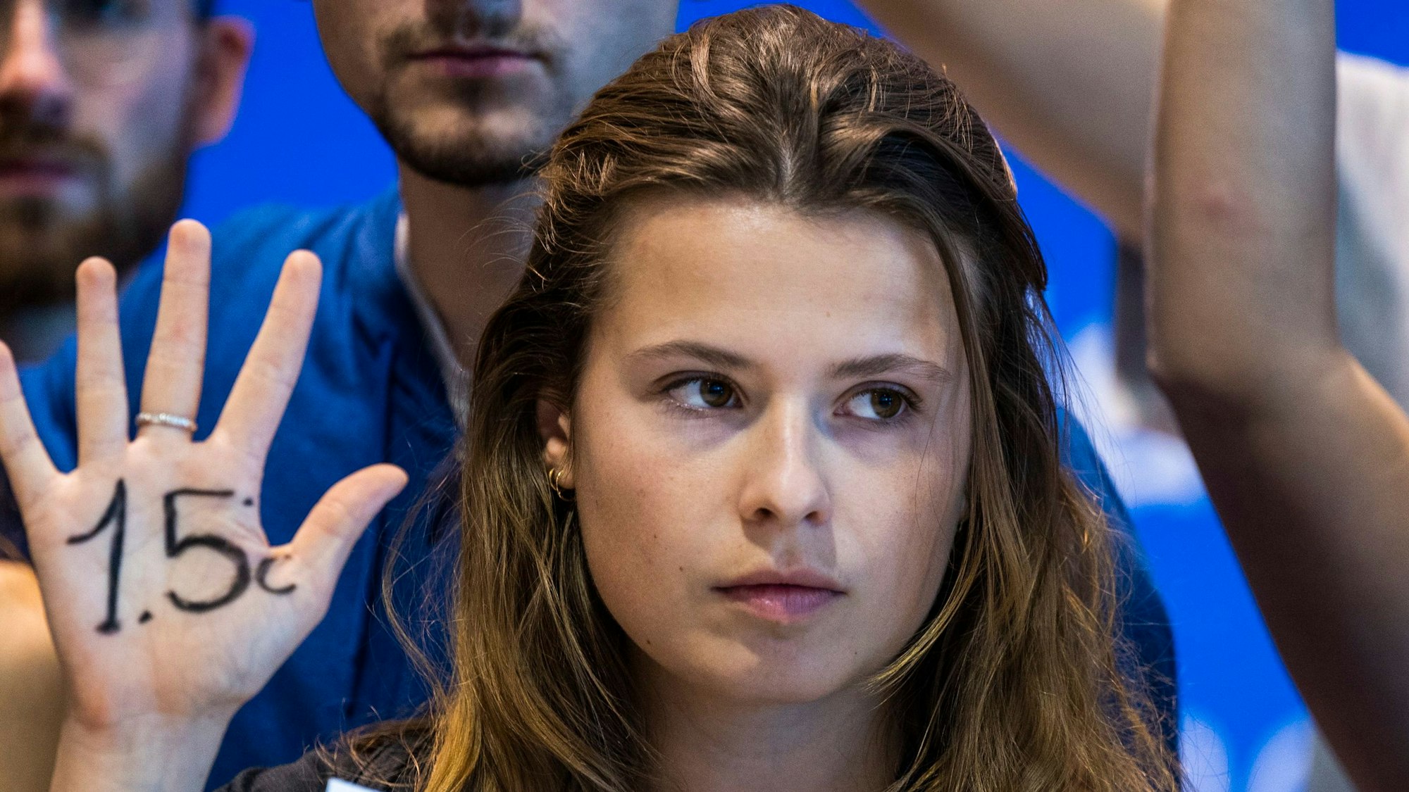 Klimaaktivistin Luisa Neubauer von „Fridays for Future“ hält eine Hand hoch, auf der „1,5 Grad“ geschrieben steht. Neubauer blickt ernst nach vorne.