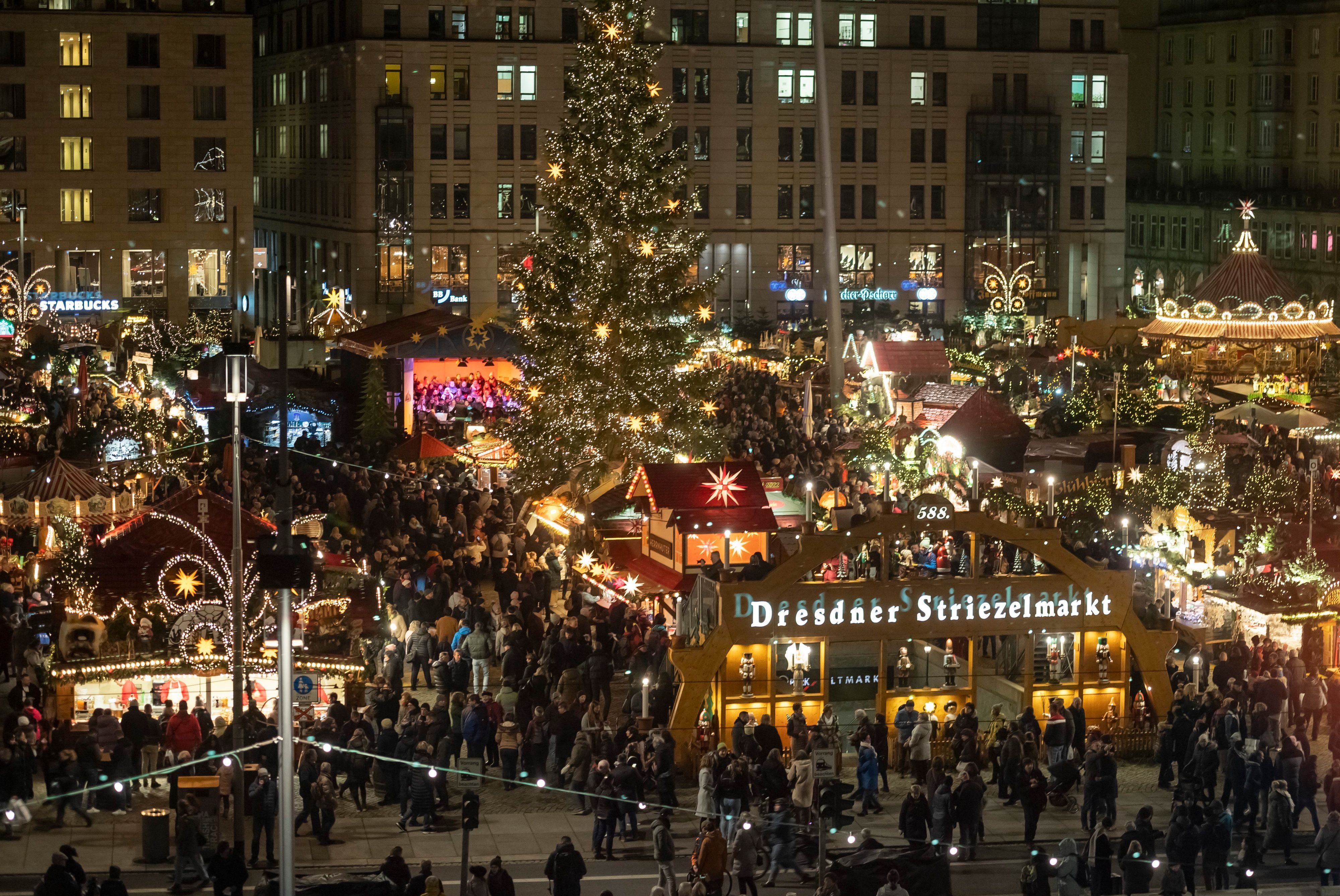 Besucher laufen zwischen festlich dekorierten Ständen und Weihnachtsbäumen über den Weihnachtsmarkt in Dresden.
