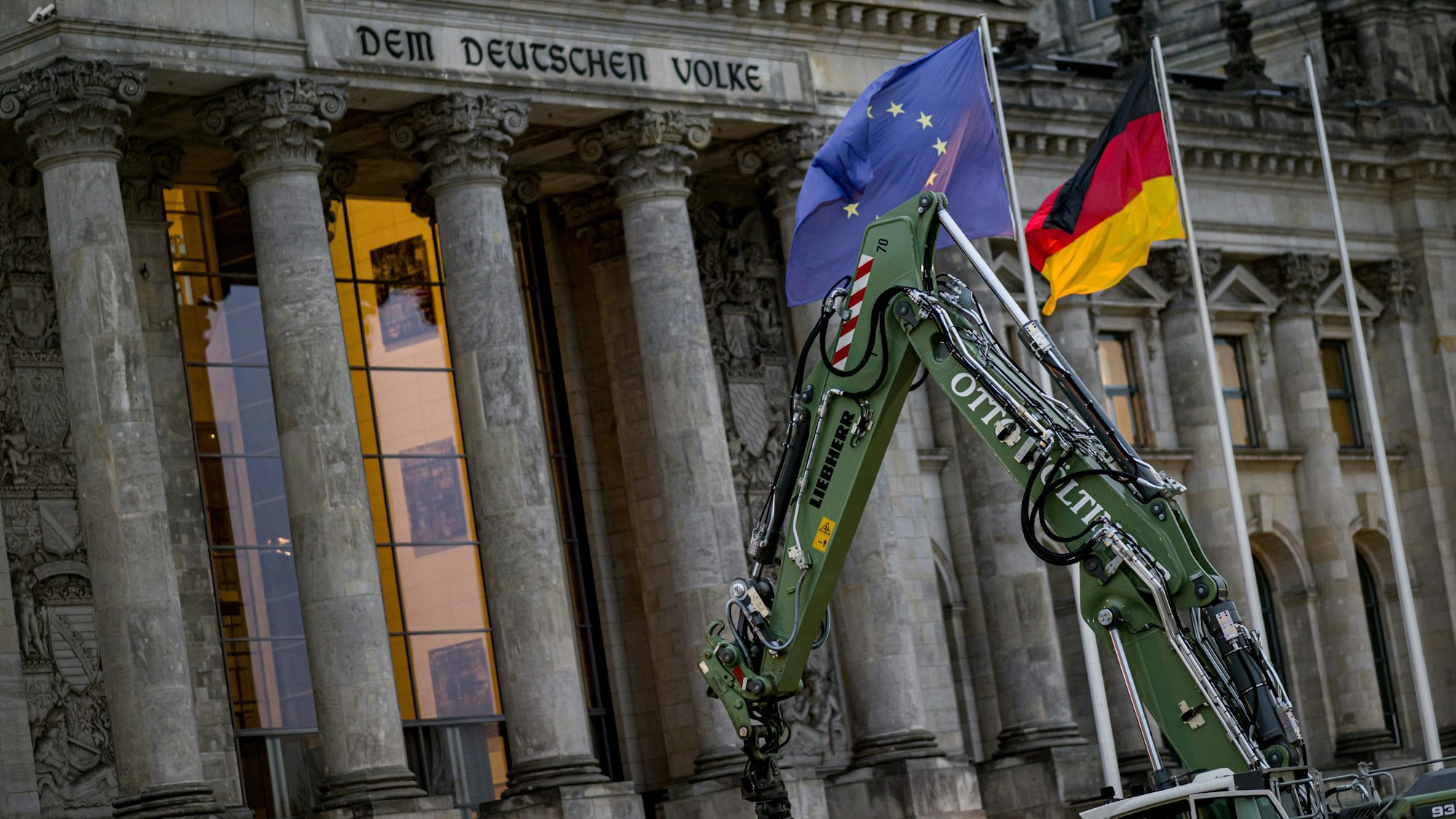 Vor dem Reichstagsgebäude in Berlin ist ein grüner Greifarm eines Baggers zu sehen.