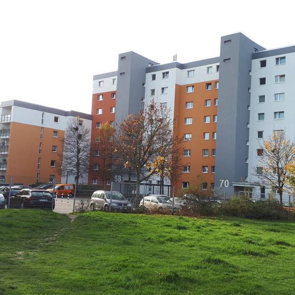 Ein grau-orangefarbener Wohnblock steht am Rande einer Rasenfläche.