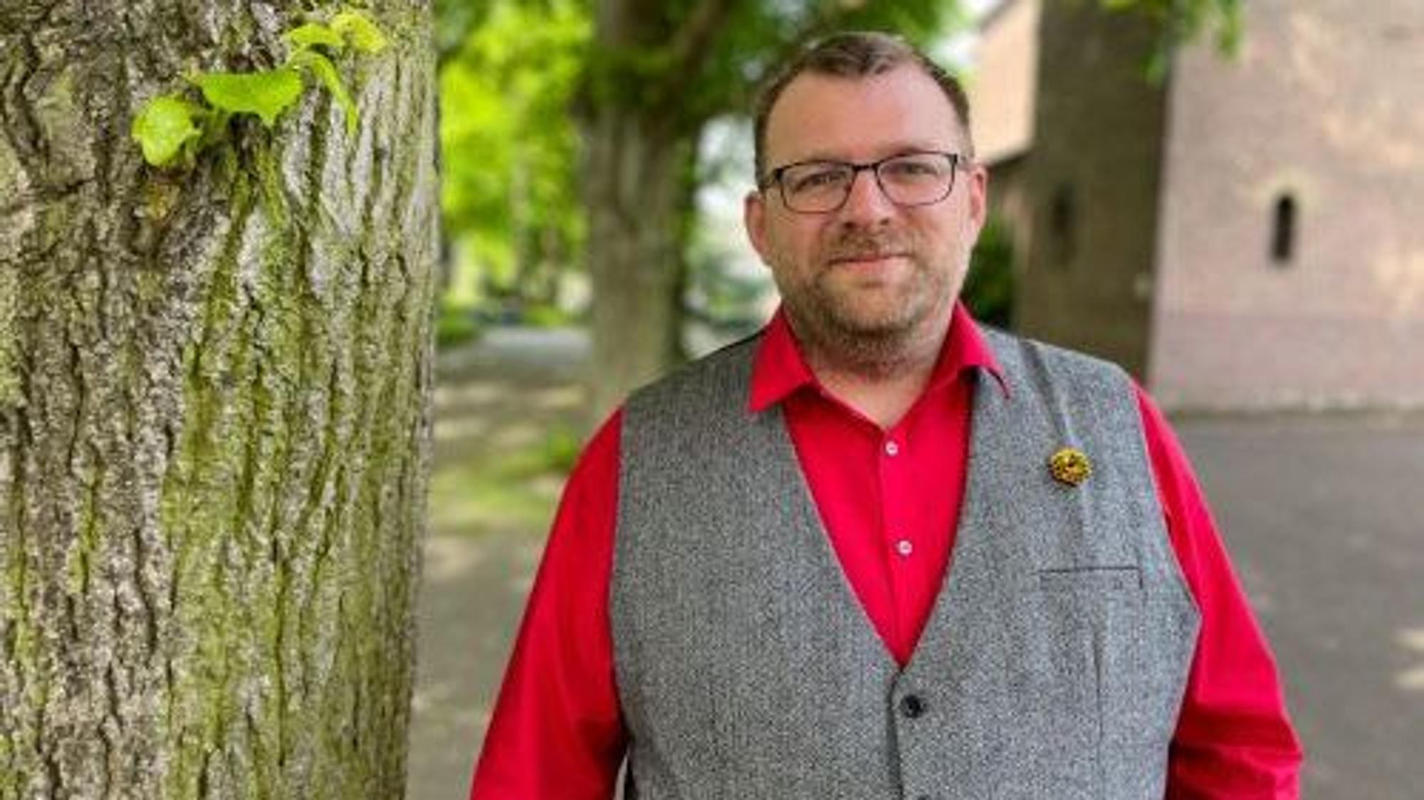 Der frühere SPD-Vorsitzende Daniel Dobbelstein steht an einem Baum, er trägt ein rotes Hemd und eine graue Weste.