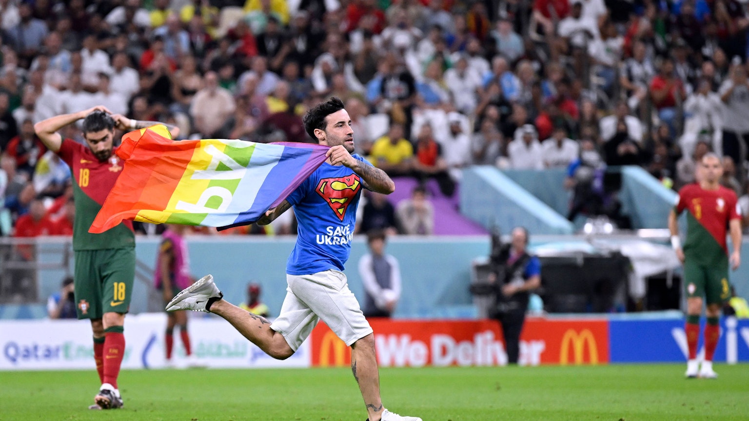 Ein Italiener rannte am Montag mit „Pace“-Regenbogenflagge auf das Feld während des Portugal-Uruguay-Spiels. Er trägt ein Superman-T-Shirt, auf dem vorne „Safe Ukraine“ und hinten „Respect for Iranien Woman“ steht.