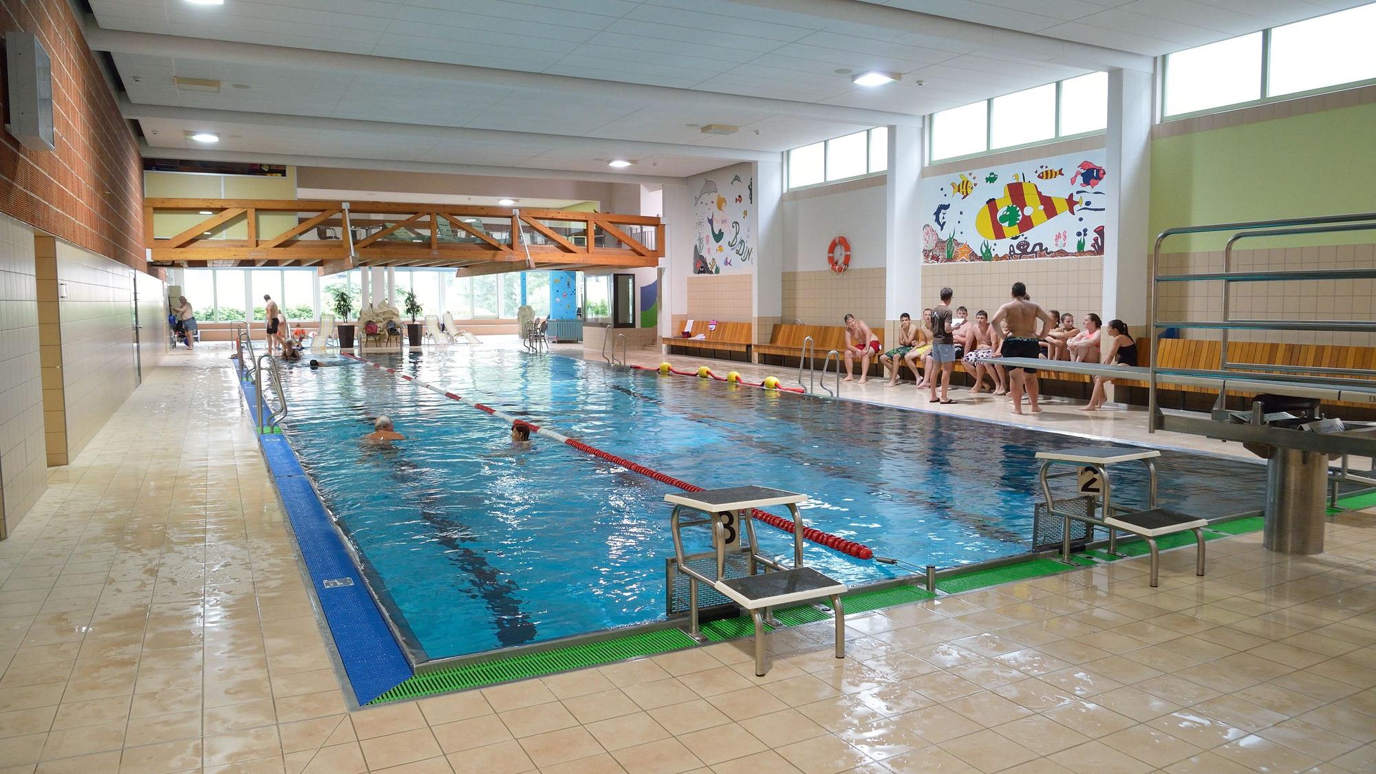 Ein Schwimmbecken an dessen Rand Kinder auf einer Bank sitzen ist zu sehen.