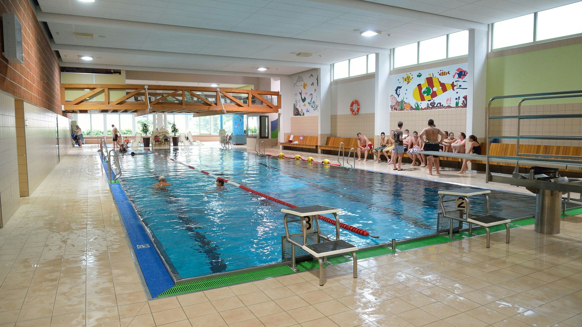 Ein Schwimmbecken an dessen Rand Kinder auf einer Bank sitzen ist zu sehen.