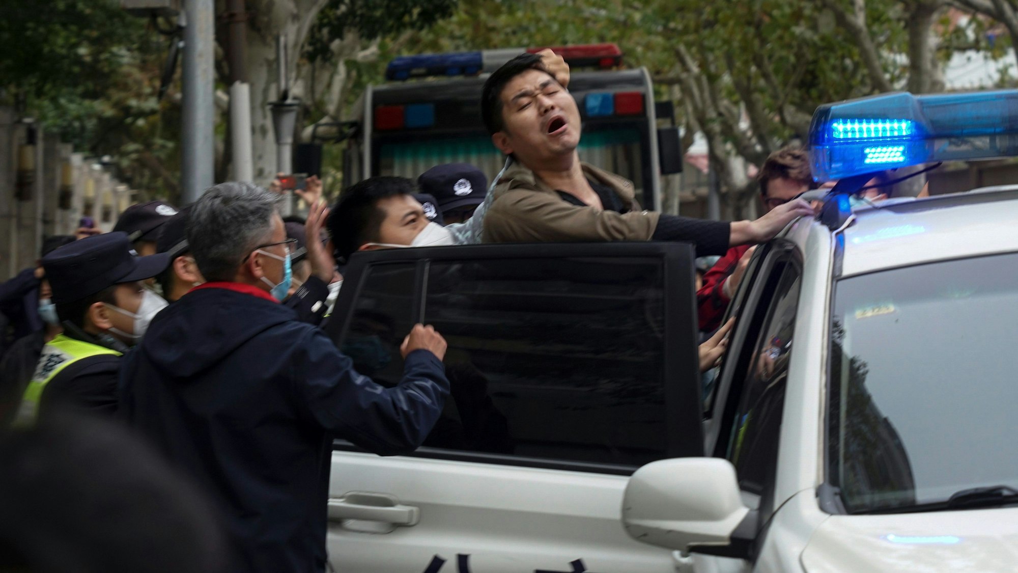 Auf diesem Foto vom Sonntag, 27. November 2022, reagiert ein Demonstrant, als er während einer Demonstration auf einer Straße in Shanghai, China, von Polizisten verhaftet wird.
