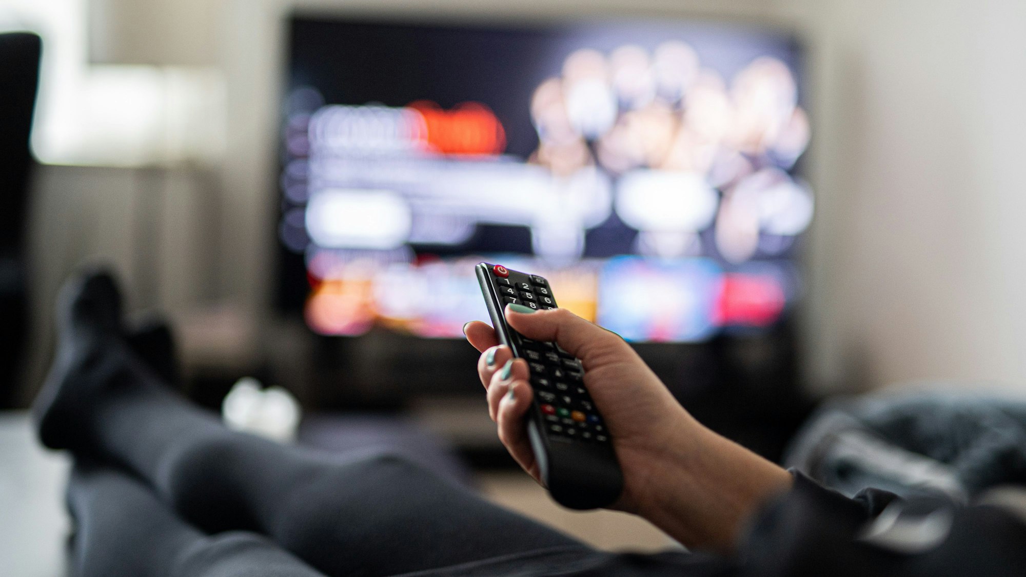 Eine Person sitzt auf einem Sofa und schaut Fernsehen. (Symbolbild)