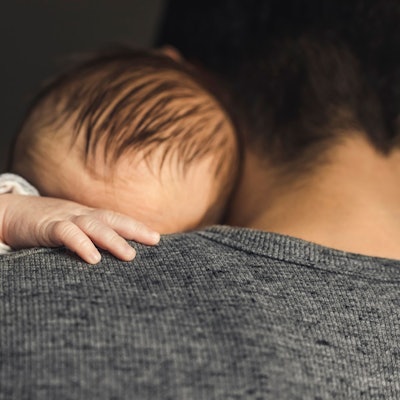 Ein Baby hat die Hand auf die Schulter des Vaters gelegt.